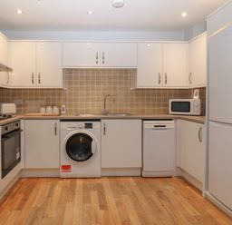 A kitchen with white cabinets a washing machine a dishwasher a microwave a refrigerator and wooden flooring at Ger Y Lli in Rhosneigr