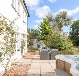 An outdoor patio area with a hot tub and seating near a white building with climbing plants at Culver Court Cottage in Venny Tedburn near Crediton