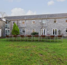 An outdoor grassy area with tables and chairs arranged in front of a stone building with multiple windows and doors at The Bevan in Bontnewydd Gwynedd