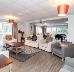 A living room with multiple armchairs and sofas around a wooden coffee table with a rug underneath at Cadwaladr in Bontnewydd near Caernarfon