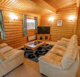 A living room with wooden walls leather sofas a coffee table a rug and a television at Bamboo Retreat in Louth
