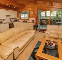 A living room with beige sofas a wooden coffee table and a kitchen with white cabinets at Bamboo Retreat in Louth