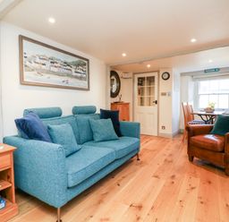 A living room with a blue sofa brown armchair wooden floor and dining table by the window at Peppers Cottage in Appledore