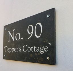 A black house number sign with white text No 90 Peppers Cottage on a white wall at Peppers Cottage in Appledore