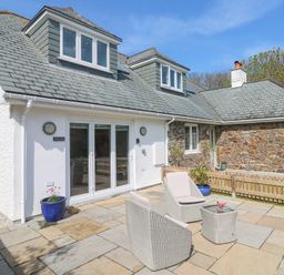 An outdoor patio area with two cushioned wicker chairs and a wicker table in front of a house at Mariners Rest in Gorran Haven