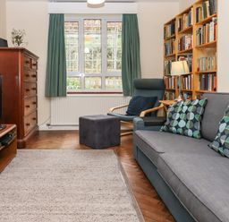 A living room with a grey couch with cushions a wooden bookshelf a blue armchair a wooden dresser and a TV at Greenhedges in Budleigh Salterton