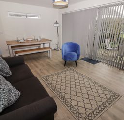 A living room with a brown sofa and cushions a blue armchair a wooden dining table with benches and a floor lamp at 16 Coedrath Park in Saundersfoot