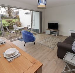 A living room with a brown sofa a blue chair a TV on a stand and a dining table set with dishes at 16 Coedrath Park in Saundersfoot
