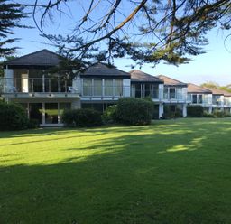 A row of modern two-story houses with balconies and glass railings overlooking a grassy lawn with bushes at 36 Coedrath Park in Saundersfoot