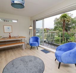 A dining area with a wooden table and benches blue armchairs and a balcony with outdoor chairs at 36 Coedrath Park Saundersfoot