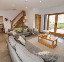 A living room with grey sofas a wooden coffee table and wooden doors leading outside at The Stables in Droitwich Spa