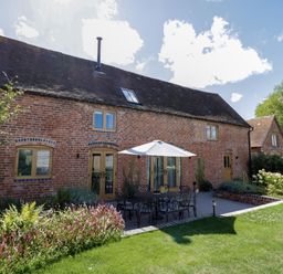 A brick house with wooden windows and doors a patio with a table umbrellas and chairs and a garden at The Stables in Droitwich Spa