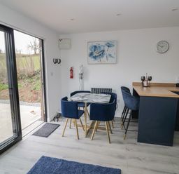 A dining area with a glass table and four blue chairs beside a kitchen counter with two bar stools at Goldthorne Lodge in Clee Hill