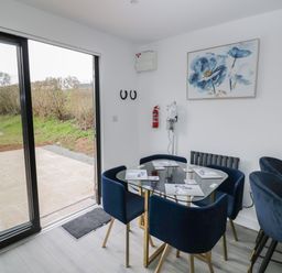 A dining area with a glass table and blue chairs next to sliding glass doors at Goldthorne Lodge in Clee Hill