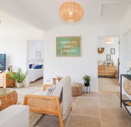 A living room with wooden furniture and plants with bedrooms visible through doorways at Polwen in Harlyn Bay Padstow