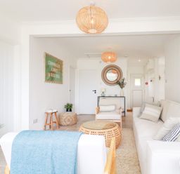 A living room with white furniture a woven coffee table and wall art at Polwen in Harlyn Bay Padstow