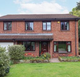 A two story brick house with a tiled roof and a front garden with flowers and bushes at Sparrow House in Alnwick