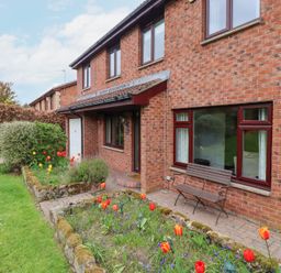 A brick house with a front garden containing flower beds and a bench at Sparrow House in Alnwick