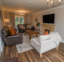 A living room with brown leather sofas a beige armchair a wooden coffee table a TV mounted above a fireplace and wood flooring at Sparrow House in Alnwick
