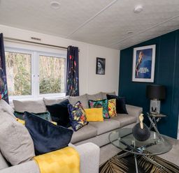 A living room with a grey sofa decorated with colorful cushions and a yellow throw blanket at The Hideout in Gilfachrheda near Llanarth