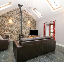 A living room with stone wall wood stove two dark leather sofas skylights and red curtains at The Old Dairy in Sarn Bach near Abersoch
