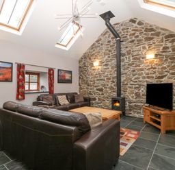 A living room with a stone wall wood burner two brown sofas a coffee table and a television at The Old Dairy Sarn Bach near Abersoch
