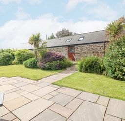 An outdoor garden with a paved patio lawn shrubs and a stone building with a door and skylights at The Old Dairy in Sarn Bach near Abersoch