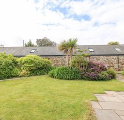 A stone cottage with a grey roof surrounded by bushes flowers and palm trees at The Old Dairy in Sarn Bach near Abersoch