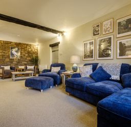 A living room with blue sofas armchairs a stone wall and framed pictures at Sunny Brae in Lindale