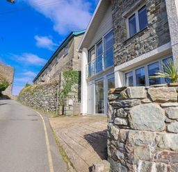 An exterior view of a house with a stone wall and road at Hafod Y Bryn in Harlech