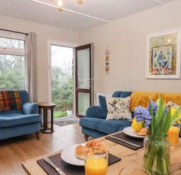 A living room with blue sofas a wooden table with flowers and orange juice at 2 The Glade in Kilkhampton