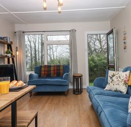 A living room with blue sofas a wooden table with orange juice and bread and a shelf with books at 2 The Glade Kilkhampton