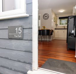 The open entrance door showing a wooden floor dining area with black chairs and a kitchen with white cabinets at 15 The Park in Kilkhampton