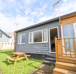 A small gray house with a wooden staircase and picnic table outside at 15 The Park in Kilkhampton