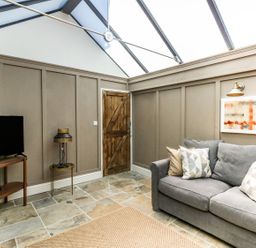 A room with a gray sofa with pillows a wooden door a flat screen tv on a wooden stand and a lamp on a small round table at The Apple Loft at Jordan House in Preston