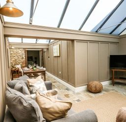 A living area with a gray sofa and cushions a dining table set with chairs a television on a wooden stand and a woven pouf at The Apple Loft at Jordan House in Preston
