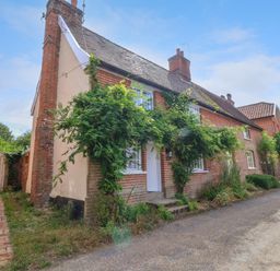 A brick cottage with plants growing on the walls and a wooden gate beside it at Brook Cottage in Peasenhall