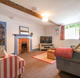 A living room with a fireplace a television striped and gray sofas and a window with red curtains at Brook Cottage in Peasenhall