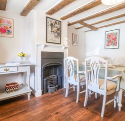 A dining room with a table and chairs a side table with a lamp and baskets and a fireplace at Brook Cottage in Peasenhall