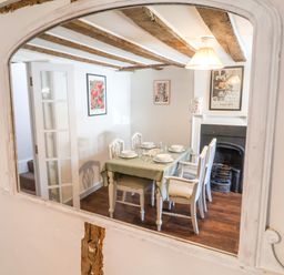 A dining room with a table set for four near a fireplace and wooden ceiling beams at Brook Cottage in Peasenhall