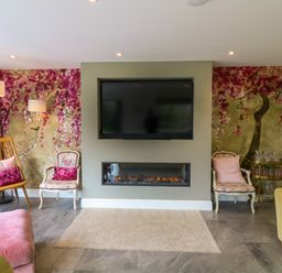 A living room with a wall mounted TV above a fireplace and floral wallpaper at Channel View House in Wadebridge