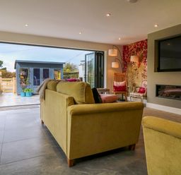 A living room with sofas a wall-mounted TV a modern fireplace and a garden shed outside at Channel View House in Wadebridge