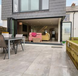 A patio with outdoor dining table and chairs leading to a living room with sofas at Channel View House in Wadebridge