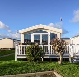 A mobile home with a white deck and patio furniture in front of a grassy area at Snape Lodge in Towyn
