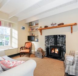 A living room with a sofa armchair wood burning stove and bookshelf at Lowen Cottage in Boscastle