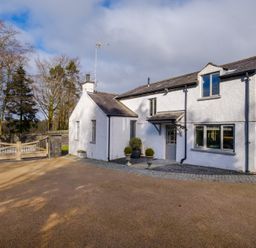 A white two-story house with a gated driveway and trees in the background at Gate House in Killington near Sedbergh