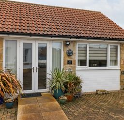 A small stone building with double glass doors and potted plants outside at The Nook in North Sunderland near Seahouses