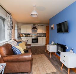 An open living space with a brown leather sofa and white cabinets in a kitchen at The Nook in North Sunderland near Seahouses