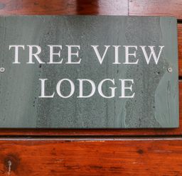 A green stone sign with the text Tree View Lodge mounted on a wooden surface at Tree View Lodge in Troutbeck Bridge