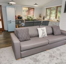 A living area with a grey sofa, dining table with chairs, kitchen appliances, and a welcome sign at Tree View Lodge in Troutbeck Bridge